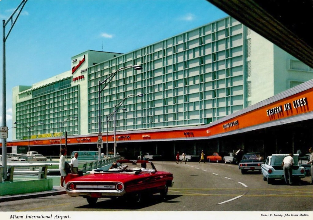 Historic view of Miami International Airport showcasing the terminal building and surrounding area, featuring classic cars and people walking.