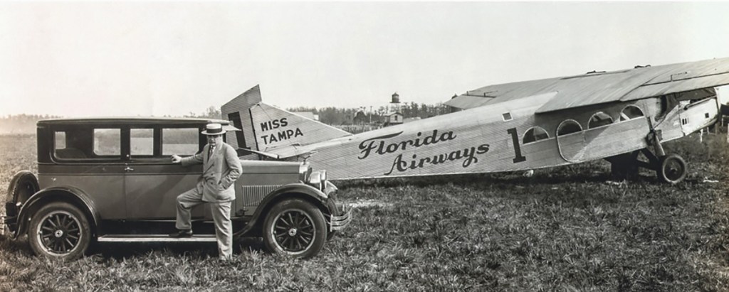 A vintage photograph featuring a man in a suit leaning against an old car with the plane 'Miss Tampa' and 'Florida Airways' visible in the background.