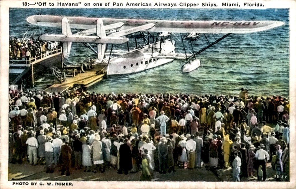 A large crowd gathered by the water to watch a Pan American Airways clipper ship, labeled 'Off to Havana,' in Miami, Florida. The vibrant scene captures the excitement of early aviation history.